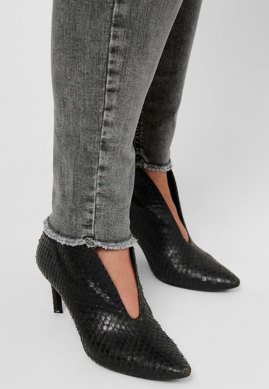 Detail van grijze jeans met rafelende zoom gedragen met zwarte puntige laarzen met slangenprint.