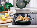 Groene koekenpan waarin twee vissen met citroen en rozemarijn worden gebakken. Op de achtergrond hangt een pan.