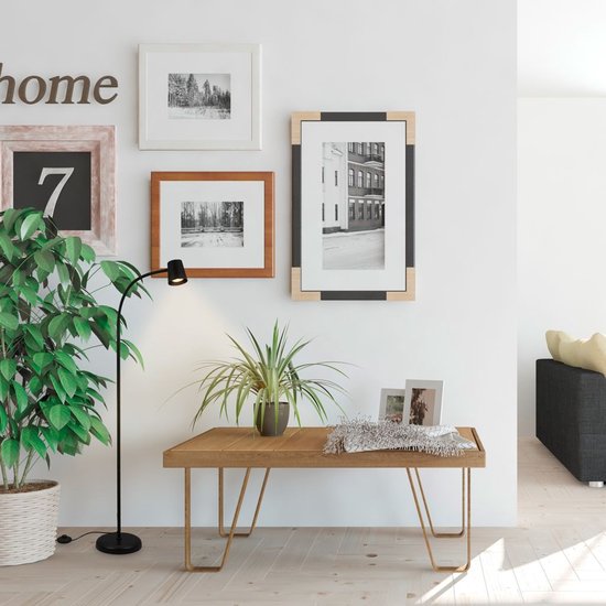 Zwarte booglamp naast een houten tafel met planten en ingelijste foto's.