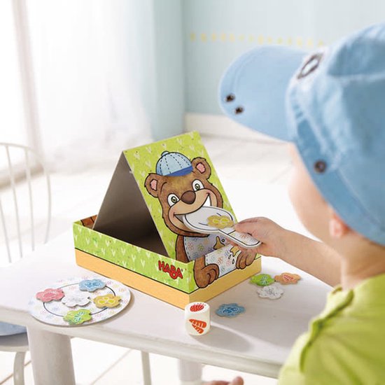 Kind met blauwe pet speelt met HABA Bärnhunger spel: beer en lepel.
