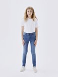 Meisje met lang blond haar, staand in een witte T-shirt en een spijkerbroek met skinny fit.