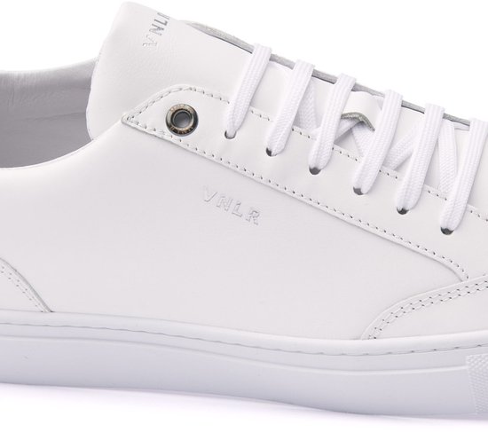 Close-up van een witte leren sneaker met zilverkleurig veteroog en VNLR-logo aan de zijkant.