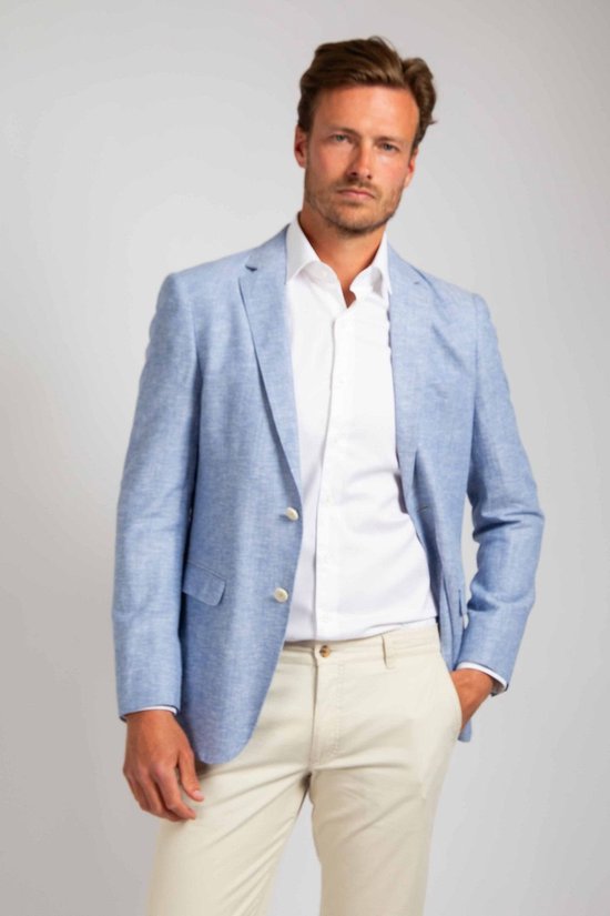 Man in lichtblauwe linnen blazer, wit overhemd en beige broek. Linkerhand in de zak.