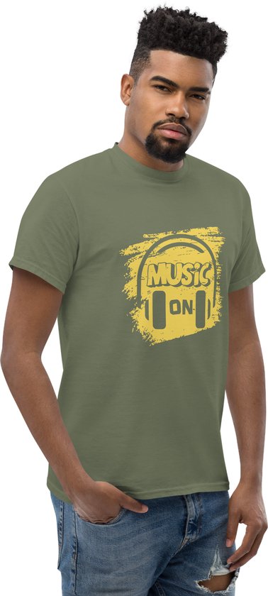 Man in een kaki groen T-shirt met gele 'Music On' koptelefoonprint. Jeans.