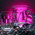 Drie glazen met verticale ribbels op een ondergrond van stenen, met roze licht.