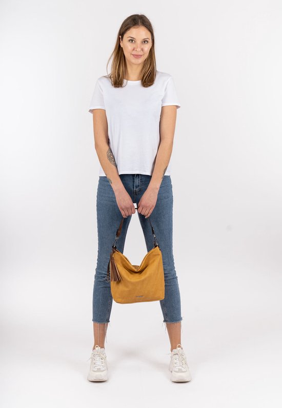 Model in wit T-shirt en spijkerbroek met een mosterdgele schoudertas met kwastjes.