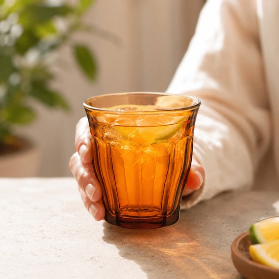 Un verre Duralex Picardie ambré avec des glaçons et une boisson rouge, à côté de raisins.