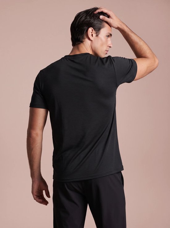 Achteraanzicht van een man in een zwart, fijn gestreept sportshirt, terwijl hij met zijn hand door zijn haar gaat.