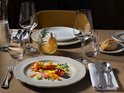 Elegant gedekte tafel met decoratief servies, kristallen glazen, bestek en een kleurrijk gastronomisch gerecht.