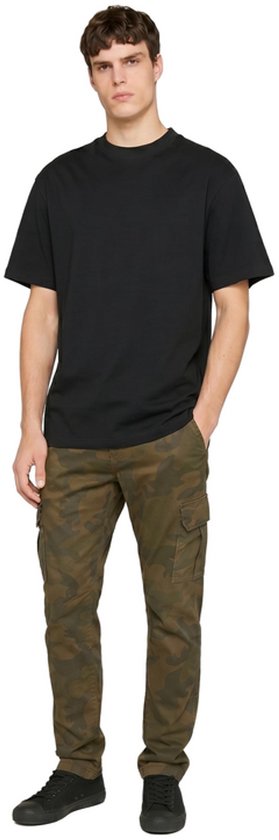 Man draagt een zwart T-shirt van Urban Classics met een camouflage cargobroek en zwarte sneakers.