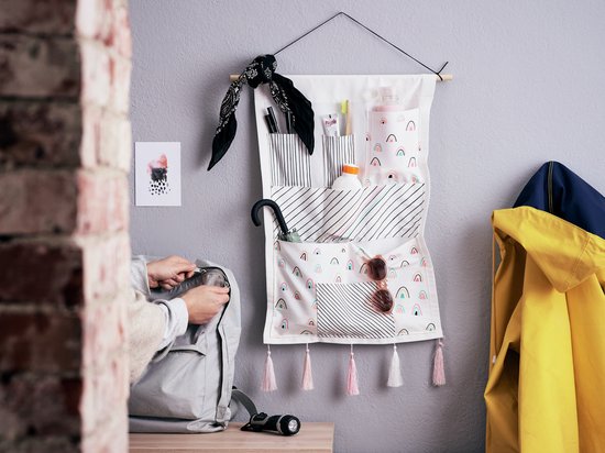 Wand organizer met vakken voor pennen, cosmetica, zonnebril. De organizer heeft regenboog- en streepjespatronen en roze kwastjes.