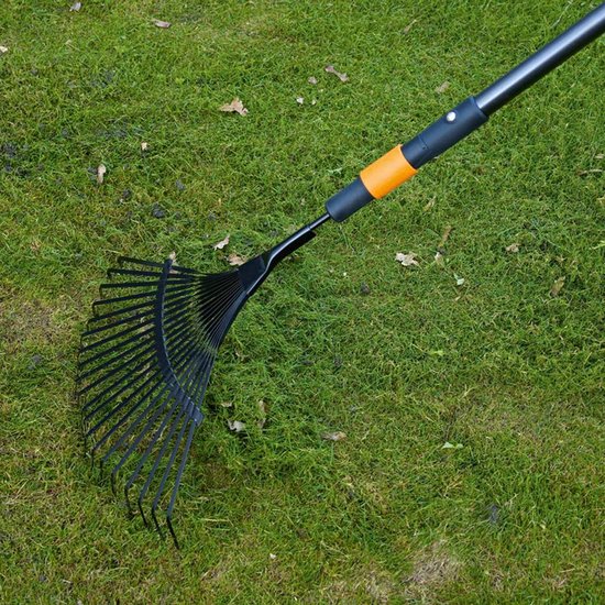 Zwarte bladhark met oranje accenten wordt gebruikt op groen gras met gevallen bladeren.