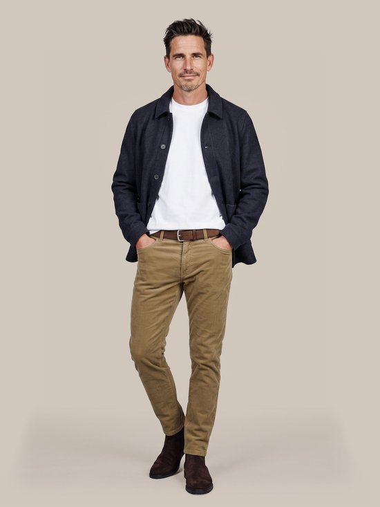 Man met donkere jas, wit T-shirt, corduroy broek in zandkleur en bruine riem.