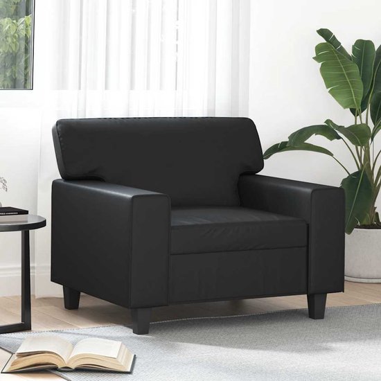 Zwarte fauteuil in een woonkamer, naast een bijzettafel met een open boek.