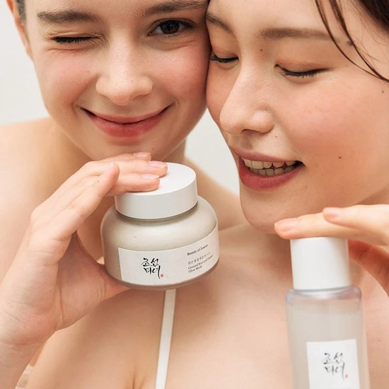 Twee vrouwen met een glimlach houden een potje en flesje Beauty of Joseon vast. De een knipoogt.