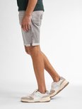 Man met grijze denim short met opgerolde broekspijpen met rode rand en sneakers.