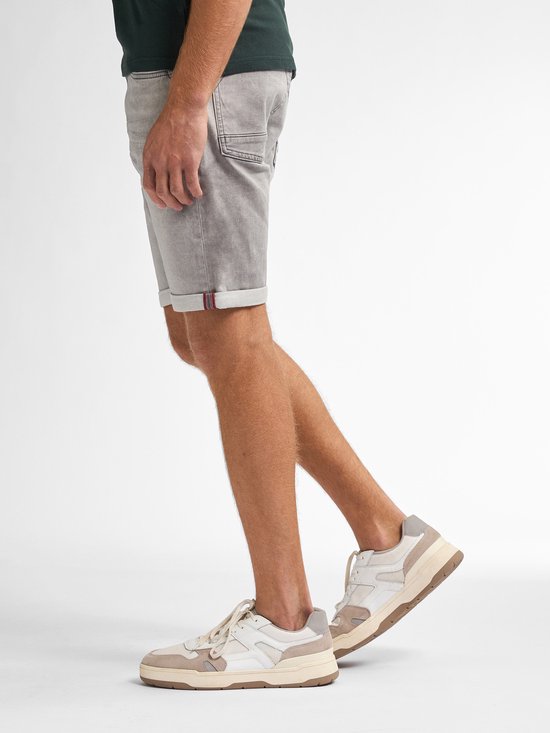 Man met grijze denim short met opgerolde broekspijpen met rode rand en sneakers.