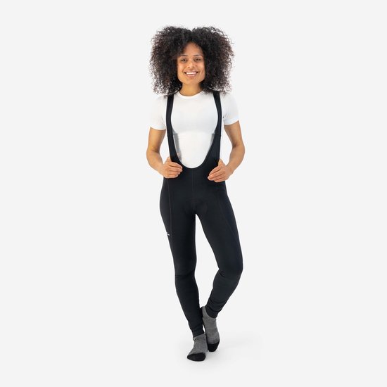 Model met krullend haar draagt een zwarte fietsbroek met bretels en witte T-shirt.