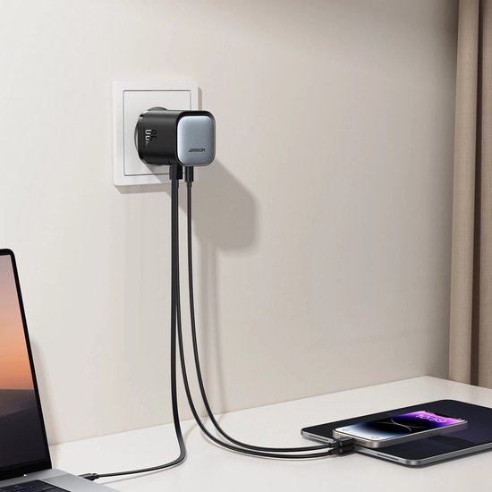 Zwarte 65W-oplader in stopcontact, verbonden met een laptop, tablet en smartphone via kabels.
