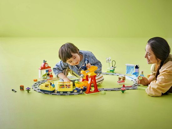 Kind en volwassene bouwen samen aan een kleurrijke LEGO DUPLO treinset op een groene ondergrond.