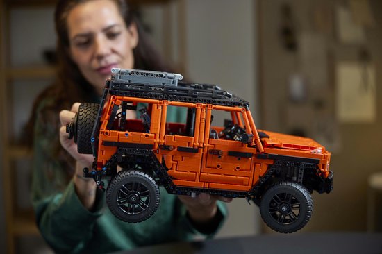 Een vrouw toont de oranje LEGO Technic Mercedes-Benz G 500, met focus op de details.