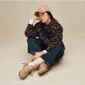 Model draagt een bruin vest met patroon, spijkerbroek, beige pet en UGG Lowmel sneakers in lichtbruin.