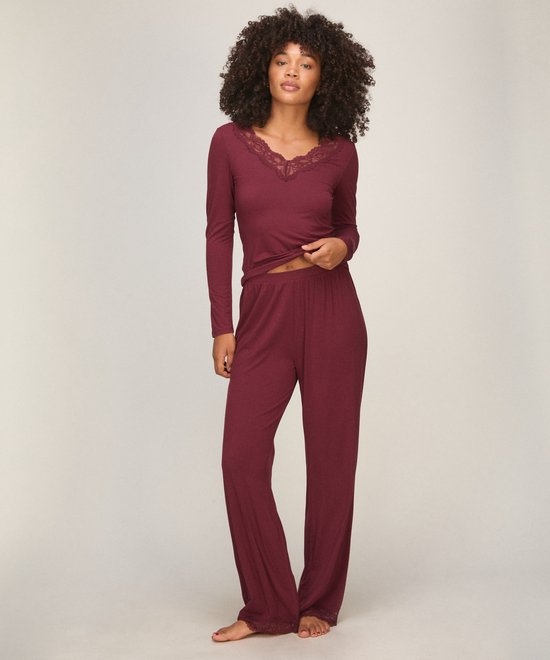 Model draagt een bordeauxrode pyjamaset met kanten details op de halslijn en broekspijpen.