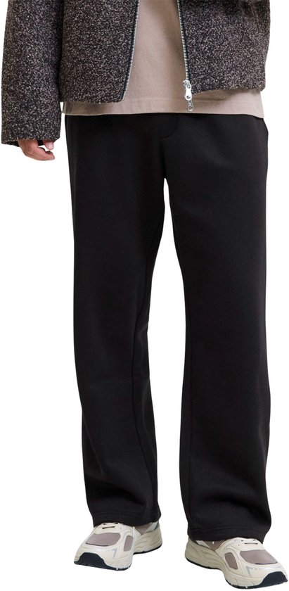 Zwarte sweatbroek met wijde pijpen, gedragen door een model met beige shirt, jas en sneakers.