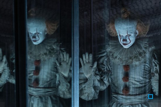 Een enge clown met wit geschminkt gezicht, rode neus en grote krans, leunend tegen glas.