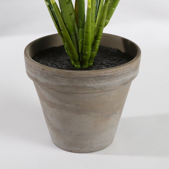 Close-up van de basis van een kunstplant met groene stengels in een verweerde bruine terracotta pot.