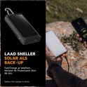 Zwarte Xtorm powerbank met zonnepaneel, karabijnhaak en indicatielampjes, naast een hand die een smartphone oplaadt.