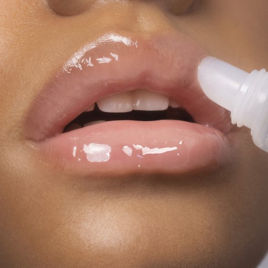 Close-up van lippen met transparante, glanzende lipgloss. De applicator brengt product aan.