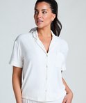 Model in wit pyjamashirt met borstzakje en kraag, met de hand in haar broekzak.