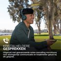 Man met groene JLab GO Lux ANC koptelefoon en telefoon in hand, lacht in de buitenlucht, met tekst 'KRISTALHELDERE GESPREKKEN'.