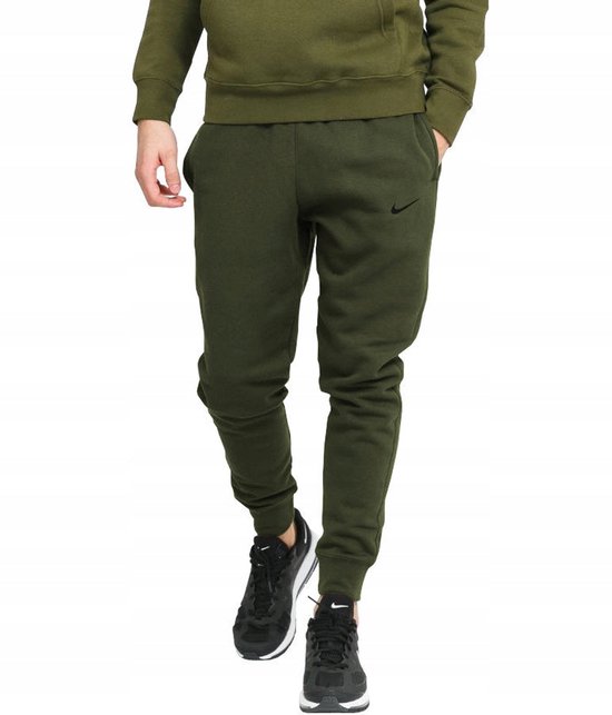 Een man in een groen Nike joggingbroek met zwarte sneakers en een groene hoodie.