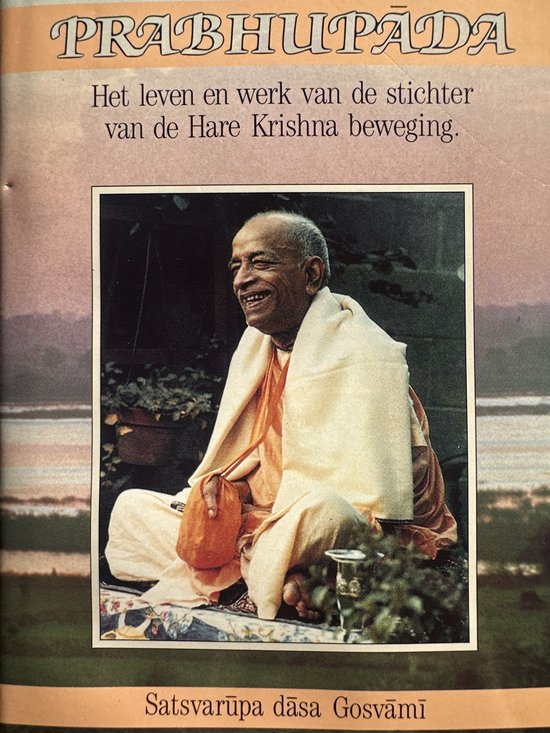 Prabhupāda, een glimlachende man in een geel gewaad en oranje sjaal, zittend in een tuin.
