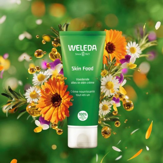 WELEDA Skin Food tube te midden van bloemen, bladeren en oliebolletjes. Groene tube met witte dop. "Voedende alles-in-één crème. Crème nourrissante tout-en-un."