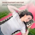 Vrouw met gesloten ogen op een beige acupressuurmat in de tuin, genietend van een rustmoment. Een roze yogamat eronder.