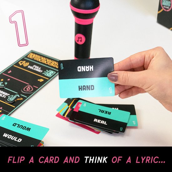 Een hand houdt de kaart 'HAND' vast bij het spel Grab the Mic. Een roze microfoon ligt naast stapels kaarten.