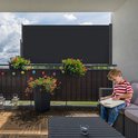 Antracietkleurig uittrekbaar scherm op een balkon waar een jongen leest.