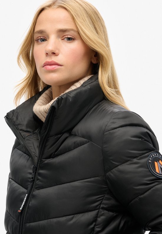 Close-up van een zwarte Superdry jas met gewatteerde banen en een rond Superdry logo.