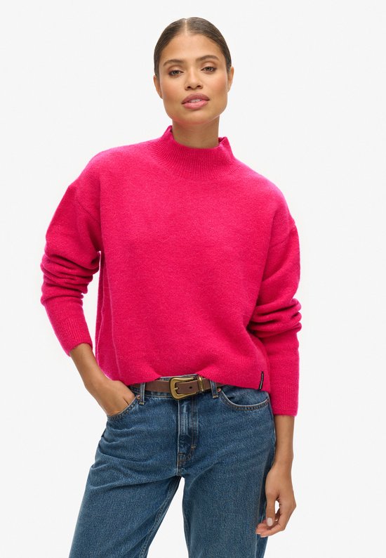 Mannequin portant un pull rose à col roulé, une ceinture marron et un jean, posant la main dans la poche.