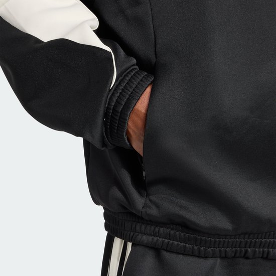 Detail van een zwarte jas met beige mouwen. Hand in de zak. Elastische zoom en manchetten.