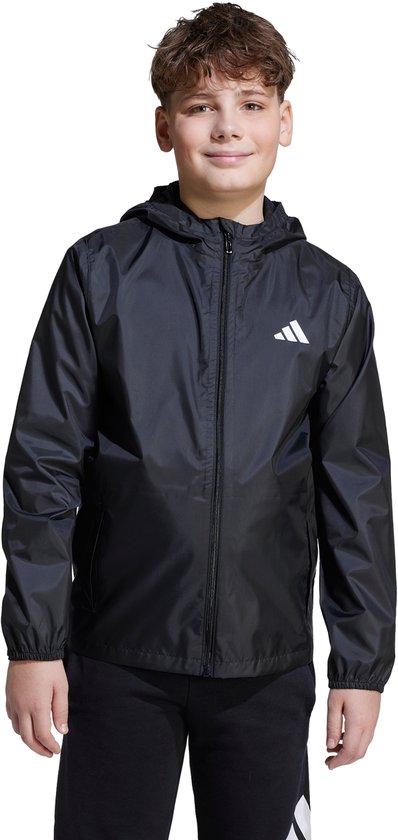 Jongen staat recht met een zwarte Adidas regenjas, capuchon en wit Adidas logo.