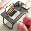 Donker houtnerf laptoptafel met laptop, bril, telefoon, boek, kopje en roze teddybeer.
