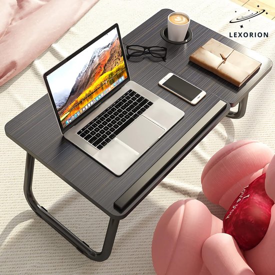 Donker houtnerf laptoptafel met laptop, bril, telefoon, boek, kopje en roze teddybeer.