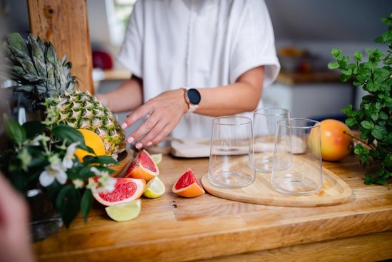 Hoge, transparante glazen op een houten plank, omringd door fruit zoals ananas, sinaasappel en grapefruit.