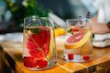 Twee doorzichtige glazen met water, grapefruit, munt, watermeloen en lavendel op een houten tafel.