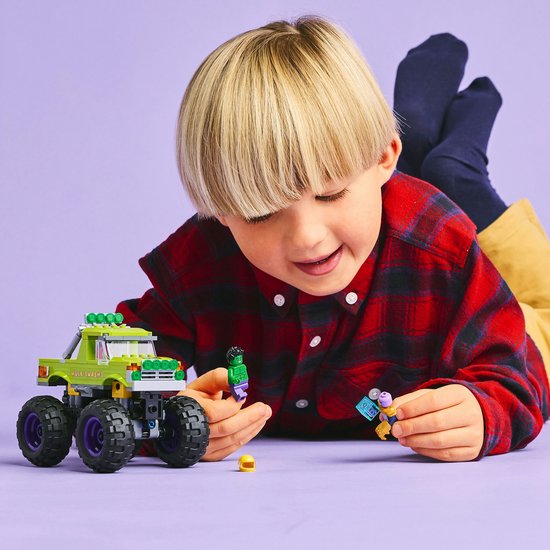 Jongen met LEGO monster truck, Hulk en paarse minifiguur op paarse achtergrond.