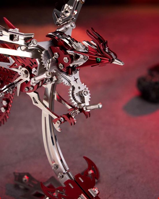 Close-up van de kop van een zilveren en rood metalen feniks model, met gedetailleerde mechanische onderdelen, tandwielen en een groen oog.